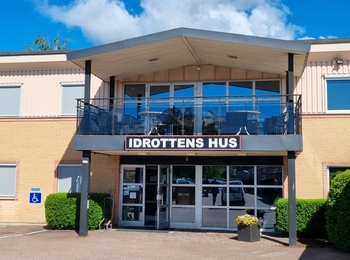 Fasaden av en byggnad med skylten 'Idrottens Hus' under en klarblå himmel.