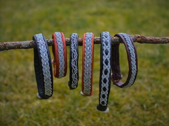 Sex armband med flätade mönster hänger på en gren utomhus med gräs i bakgrunden.