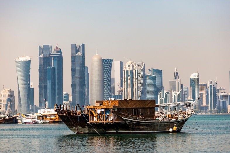 Traditionell träbåt på vattnet med moderna skyskrapor i bakgrunden, troligen Doha, Qatar.