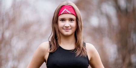 Ung kvinna med röd bandana och röda byxor står utomhus med händerna i midjan.