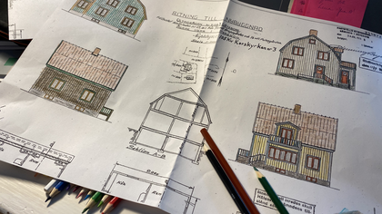 Färglagda arkitektritningar av ett hus ligger på ett bord med färgpennor bredvid.
