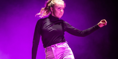 En person dansar barfota på en scen med lila ljus och rökeffekter.