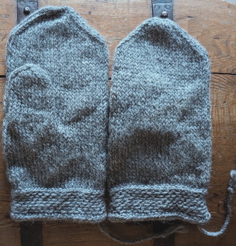 Två grå tumvantar i tekniken tvåändsstickning 