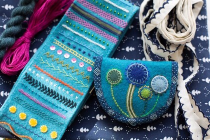 Broderade textilier i blå och turkosa nyanser, inklusive en liten väska och band, på ett mönstrat tyg.
