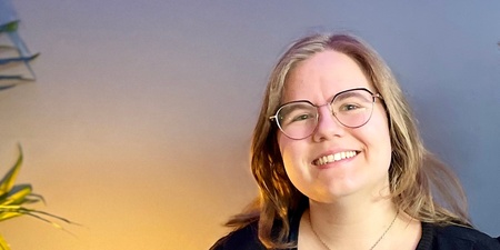 Två leende personer sitter tillsammans i en blå soffa i ett rum med blå vägg och grön växt.