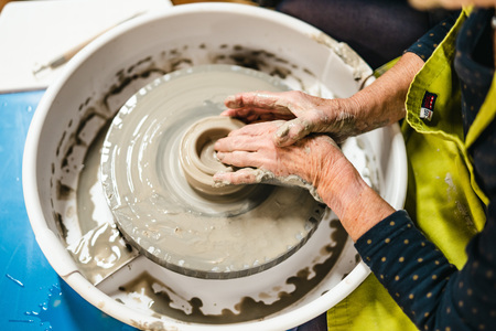 En person formar lera på en drejskiva med händerna, omgiven av vatten och lerskvätt.