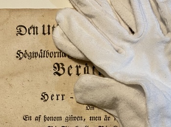 Ett gammalt svenskt dokument från 1768 med vita handskar ovanpå, liggande på ett bord.