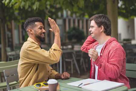 Två personer sitter utomhus vid ett bord och studerar. De lyfter händerna för att göra high five.