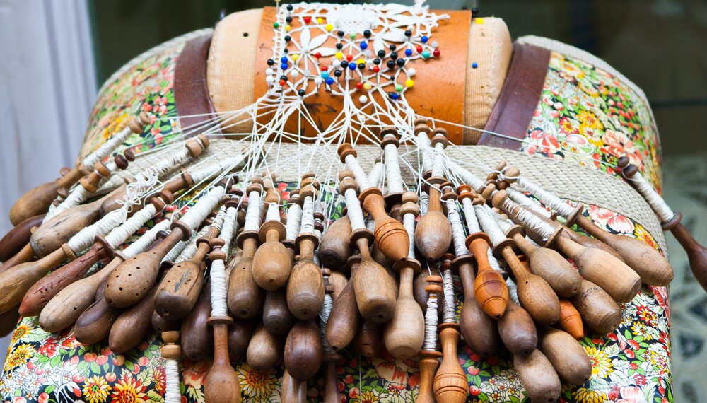 Närbild av knyppeldyna med träspolar och spetsarbete i vitt garn.