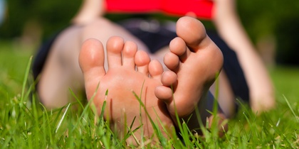 En person ligger på gräset och läser en röd bok, bara fötterna syns tydligt i förgrunden.