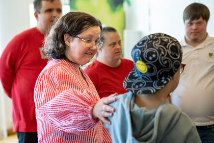 En grupp personer, några med Downs syndrom, står tillsammans inomhus och samtalar.