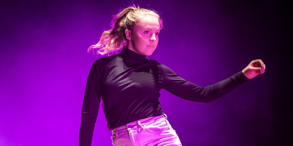 En person dansar barfota på en scen med lila ljus och rökeffekter.