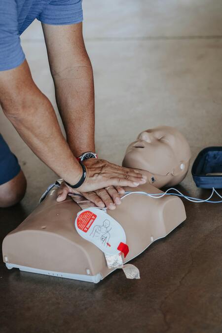 Person övar hjärt-lungräddning på en docka med hjälp av en defibrillator.