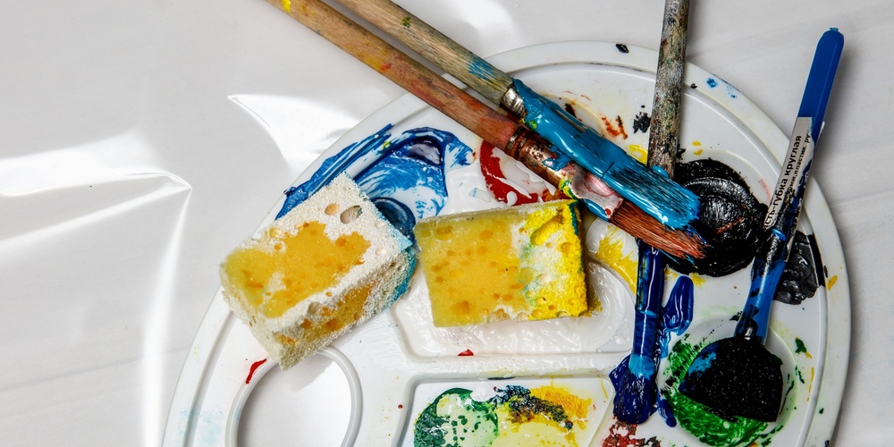 En konstnärspalett med färgglada färger, penslar och svampar på en vit bakgrund.