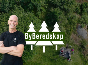 Man ler framför en skogsbakgrund med texten 'ByBeredskap' och tre vita granar.