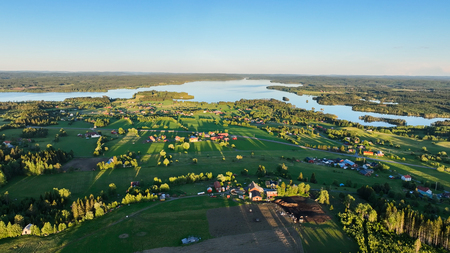 Landskapsvy över gröna fält, gårdar och sjöar under klarblå himmel.