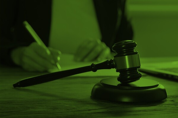 En person sitter och skriver på ett papper. I förgrunden ligger en styrelseklubba.