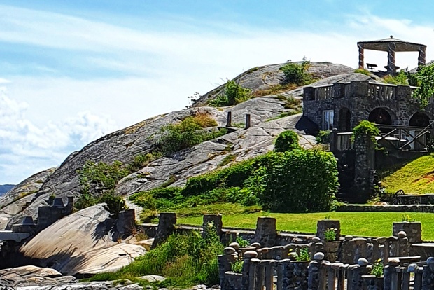 Stenbyggnader och valv på en grön kulle vid havet under en klarblå himmel.