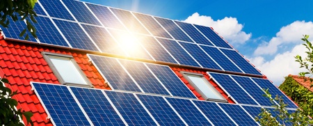 Solpaneler installerade på ett rött hustak under en klarblå himmel med solsken.