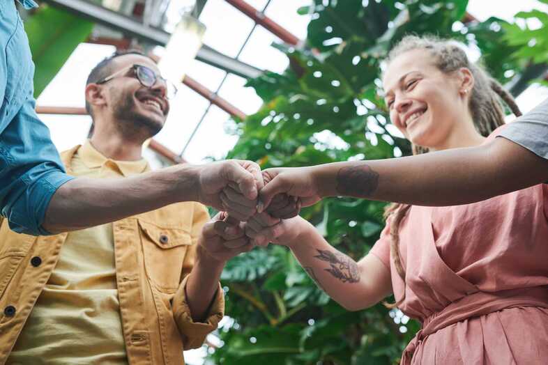 Fyra personer står i ett växthus, sträcker fram händerna mot varandra boxar varandras händer.