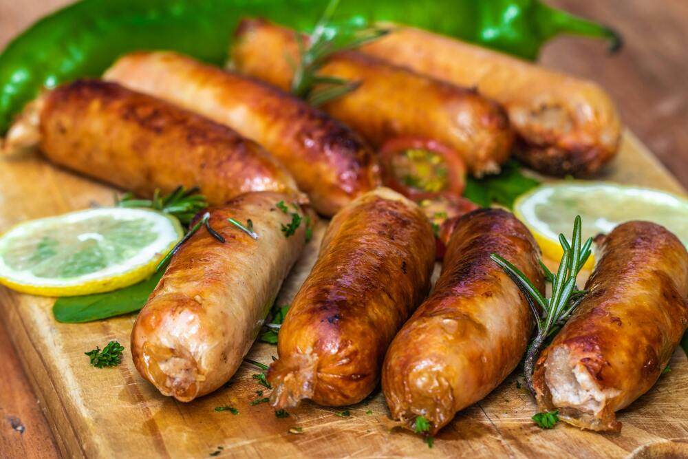 Grillade korvar ligger på en träbricka med citronskivor, örter och grön chili.