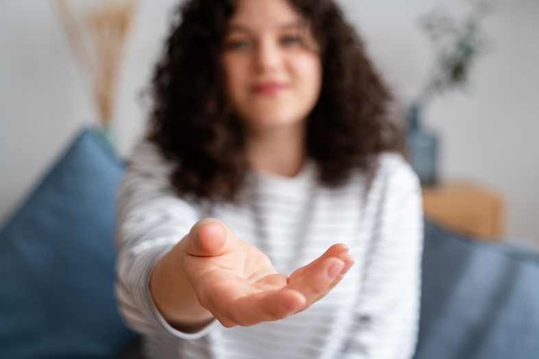 En person i randig tröja sträcker ut handen mot kameran i en hemmiljö.