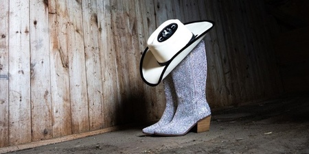 Ett par glittriga cowboyboots med en cowboyhatt ovanpå står på ett trägolv i en gammal lada.