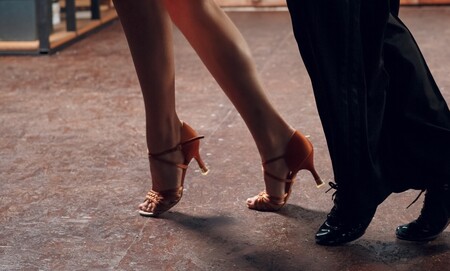 Två personer dansar, endast deras ben och fötter i dansskor syns på ett dansgolv.