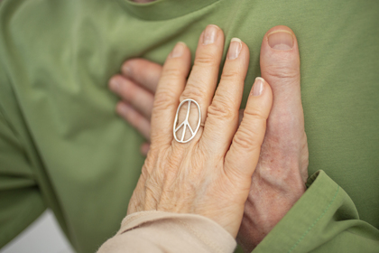 Två händer, en med en fredssymbolring, vilar på ett bröst med grön tröja i en lugn gest.