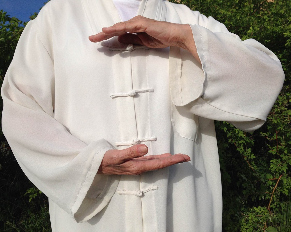 Person i vit traditionell dräkt utför en tai chi-rörelse med händerna utsträckta framför kroppen.