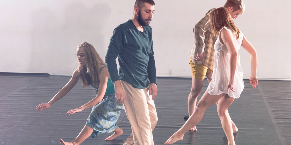Fyra personer dansar barfota på ett svart golv i en ljus dansstudio.