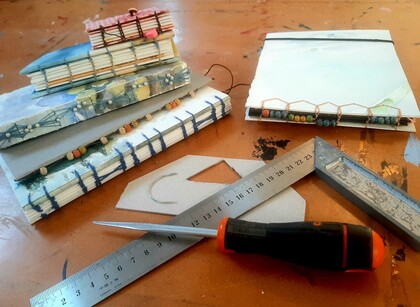 Handgjorda anteckningsböcker, verktyg och material för bokbindning på ett arbetsbord.