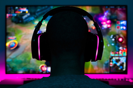 En person med hörlurar sitter framför en datorskärm och spelar ett färgglatt datorspel.