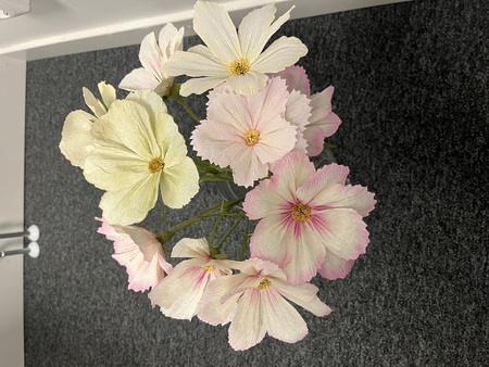 En bukett ljusa, konstgjorda blommor av papper i rosa och vitt står på ett grått golv.