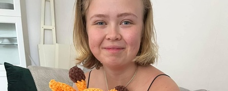 Ung kvinna sitter i soffa och håller i en stickad giraff-leksak, ler mot kameran.