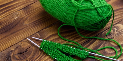 Grönt garnnystan och stickning på träbord med två stickor och påbörjat arbete.