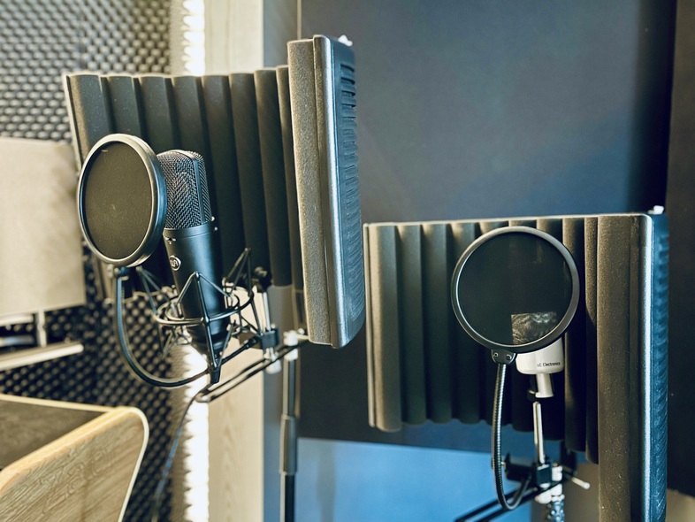 Två mikrofoner med popfilter och ljudisolerande skärmar i en inspelningsstudio.