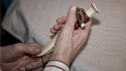 Två händer håller en liten dekorativ kniv med slida, liggande på ett bord med vit duk.