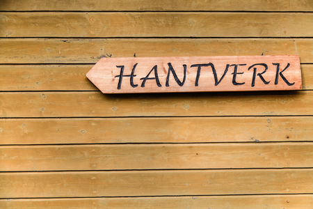 Träskylt med texten 'HANTVERK' på en trävägg.
