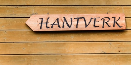 Träskylt med texten 'HANTVERK' på en trävägg.