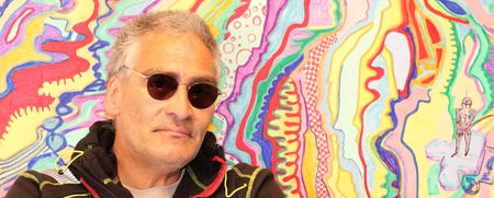 Man med solglasögon står framför en färgglad, abstrakt målning med vågiga mönster.