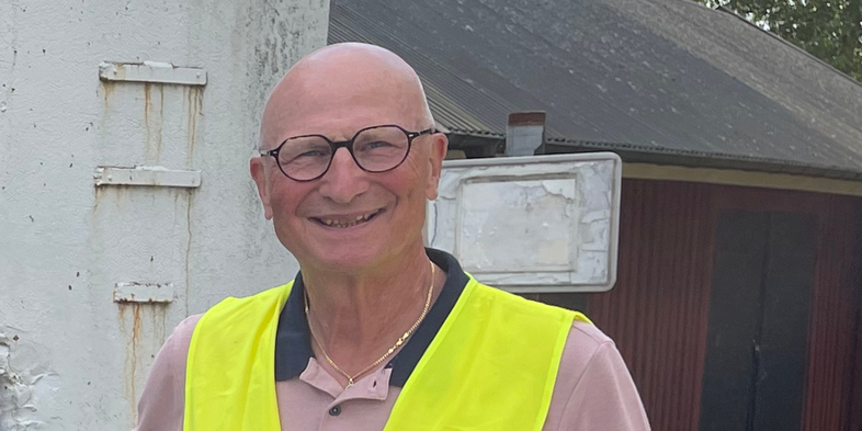 Fyra män står utomhus framför en vit vägg med hål, två bär gula reflexvästar.