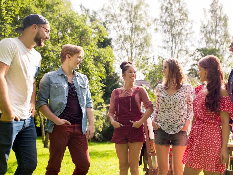 Sex unga vuxna står utomhus i en park och pratar med varandra en solig dag.
