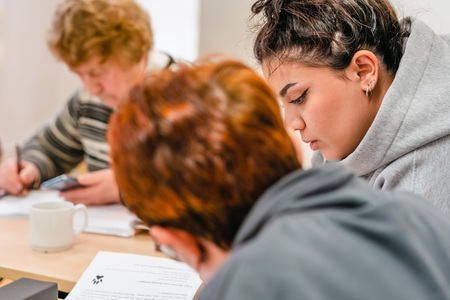 Tre personer sitter vid ett bord och studerar tillsammans, fokus på en ung kvinna i grå tröja.