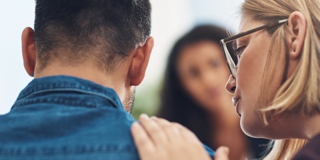 En kvinna tröstar en man genom att lägga handen på hans axel i en stödjande miljö.