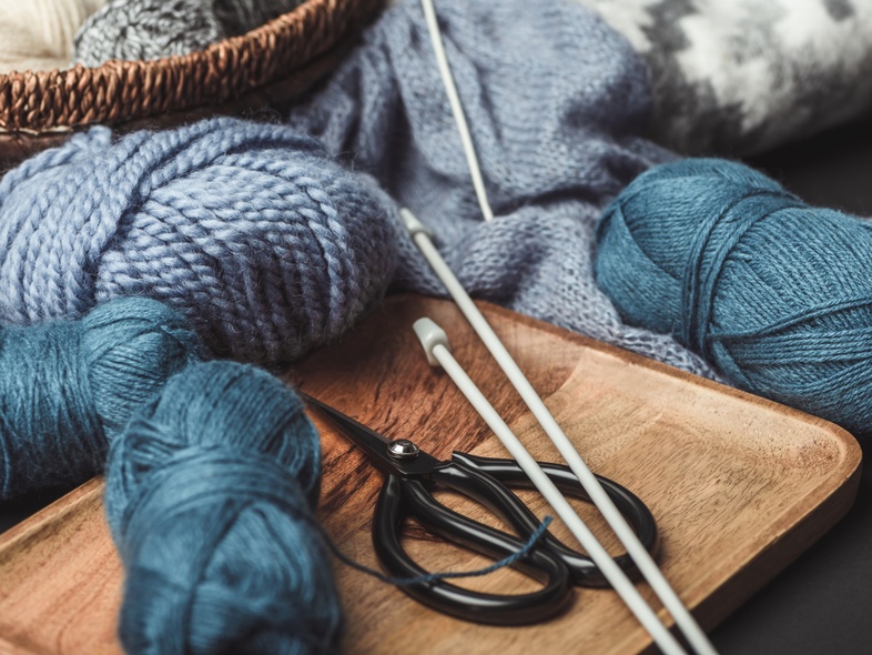 Garnnystan, stickor och sax ligger på en bricka och i en korg, redo för stickning.