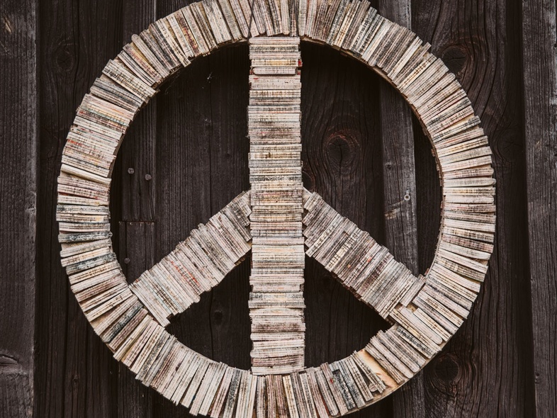 En stor fredssymbol gjord av träbitar hänger på en mörk trävägg.