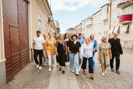 En grupp vuxna människor går tillsammans på en stadsgata med bostadshus i bakgrunden.