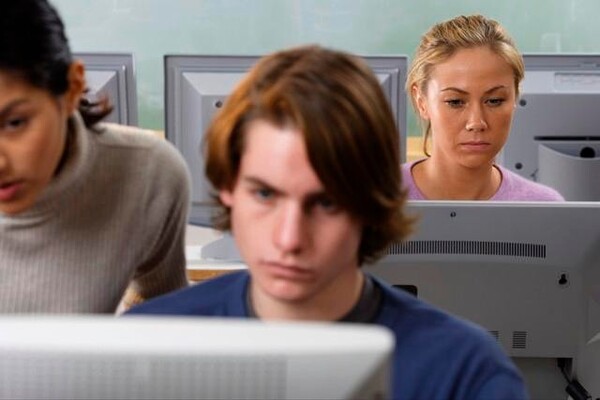 Tre personer arbetar framför datorer i ett klassrum.