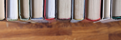 Böcker stående på rad, fotograferade ovanifrån med fokus på bokryggarna och träbordet under.